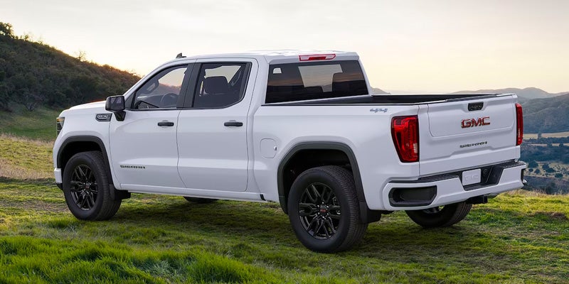 White Sierra 1500 parked on grassy area surrounded by mountains